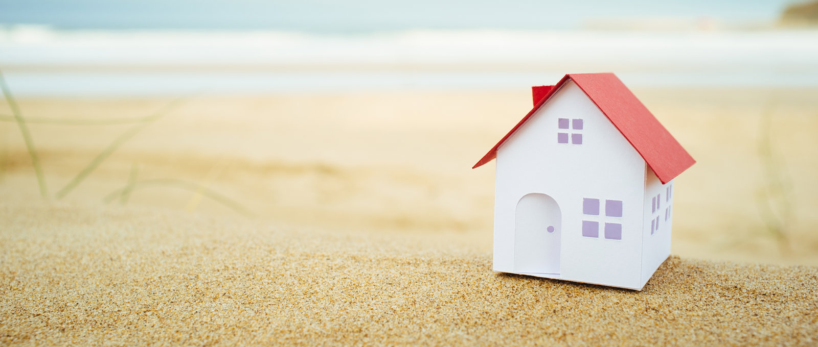 A model of a house sat on a sandy beach.