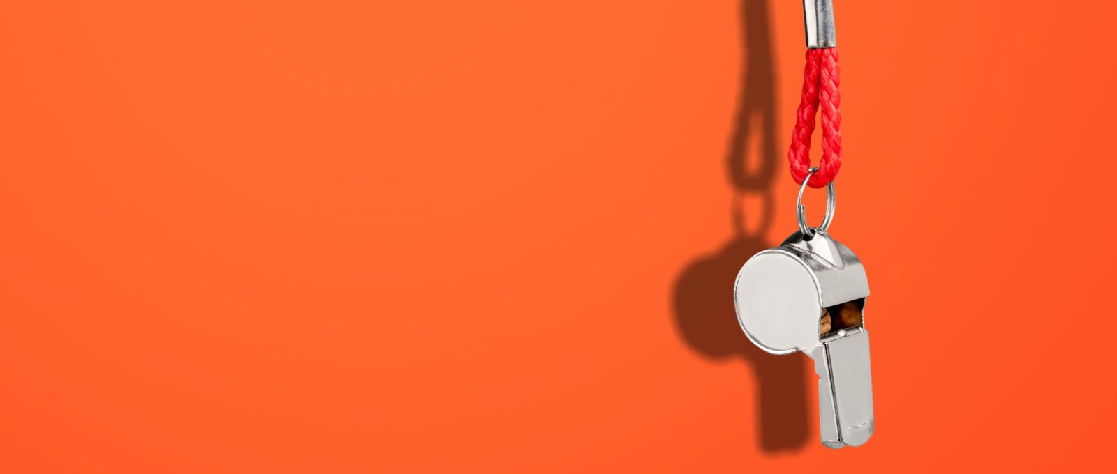 A metal whistle dangling on a red cord in front of a red background