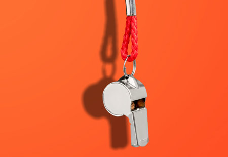A metal whistle dangling on a red cord in front of a red background