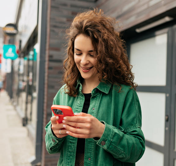 Outdoor Portrait Lovely Stylish Girl With Curls Wearing Green Shirt Using Smartphone With Smile Carefree Young Caucasian Girl Is Using Modern Smartphone Standing Outdoors