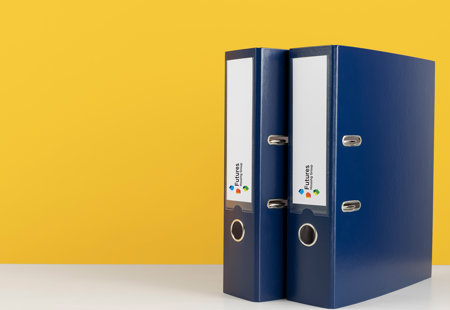 Photo of two blue binder files on a white surface with a yellow background. The spines of the files have a white area with the Futures Housing Group logo on it.