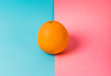 Photo of an orange on a background that if half turquoise and half pink. The orange sits on the dividing line. 