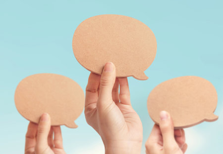 close-up of three hands holding up blank wooden speech bubbles against a pale blue sky