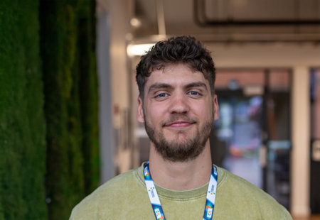 Close-up photo of a man smiling stood next to a green wall