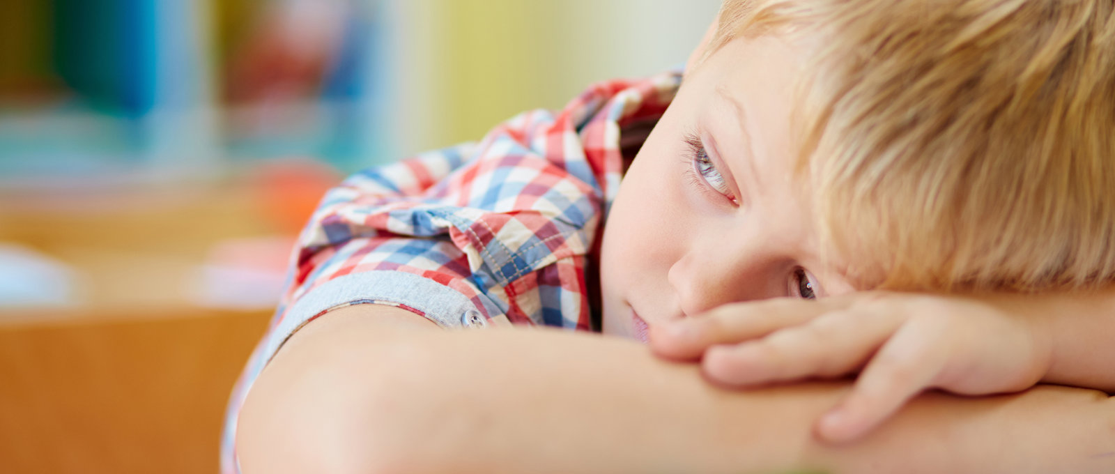 Photograph of a young boy resting his head on his arms on a table and looking sad
