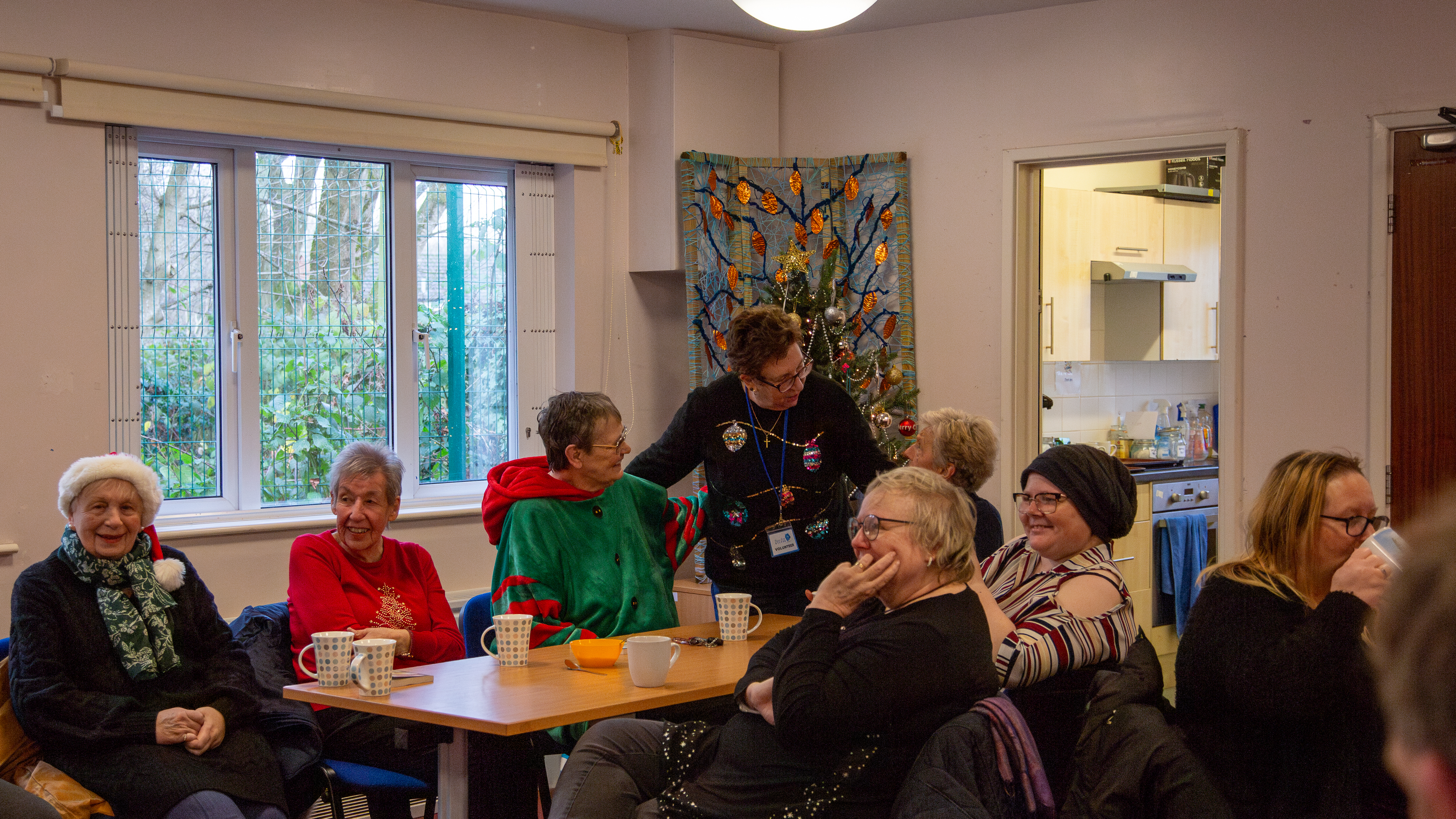 A community group wearing Christmas jumpers, chatting around a table