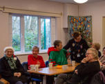 A community group wearing Christmas jumpers, chatting around a table