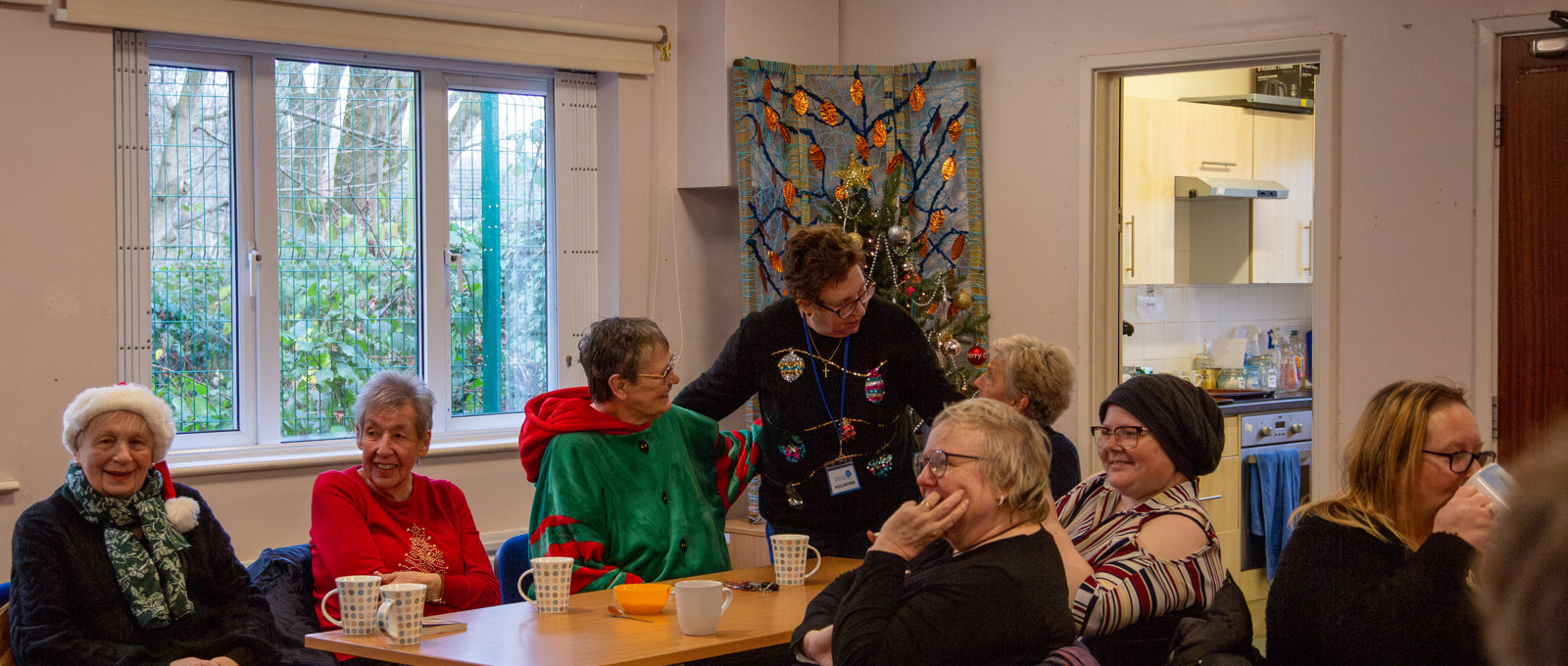 A community group wearing Christmas jumpers, chatting around a table