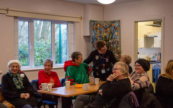 A community group wearing Christmas jumpers, chatting around a table