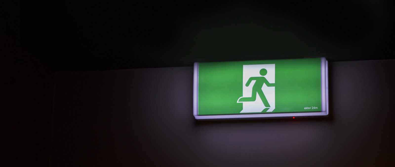A green emergency exit sign against a black wall