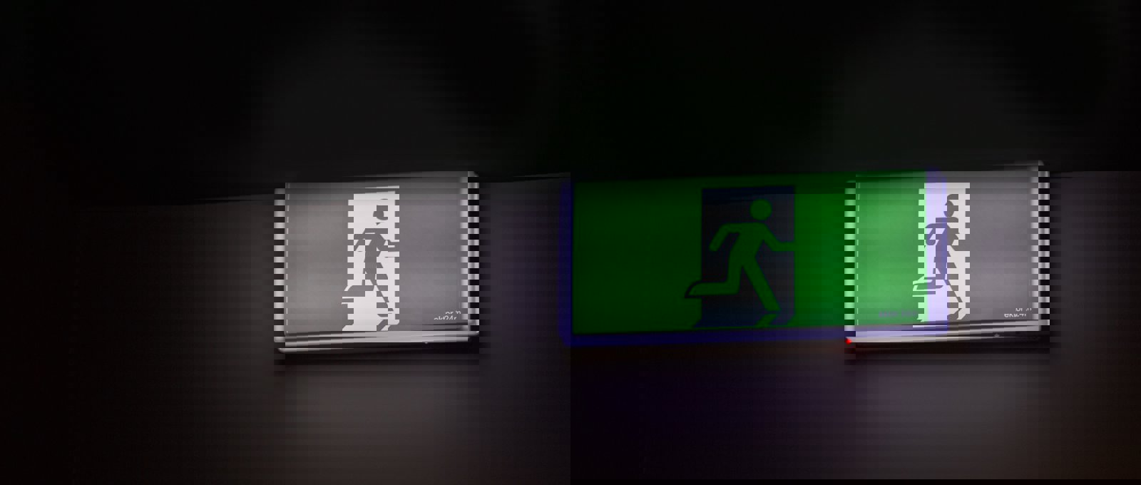 A green emergency exit sign against a black wall