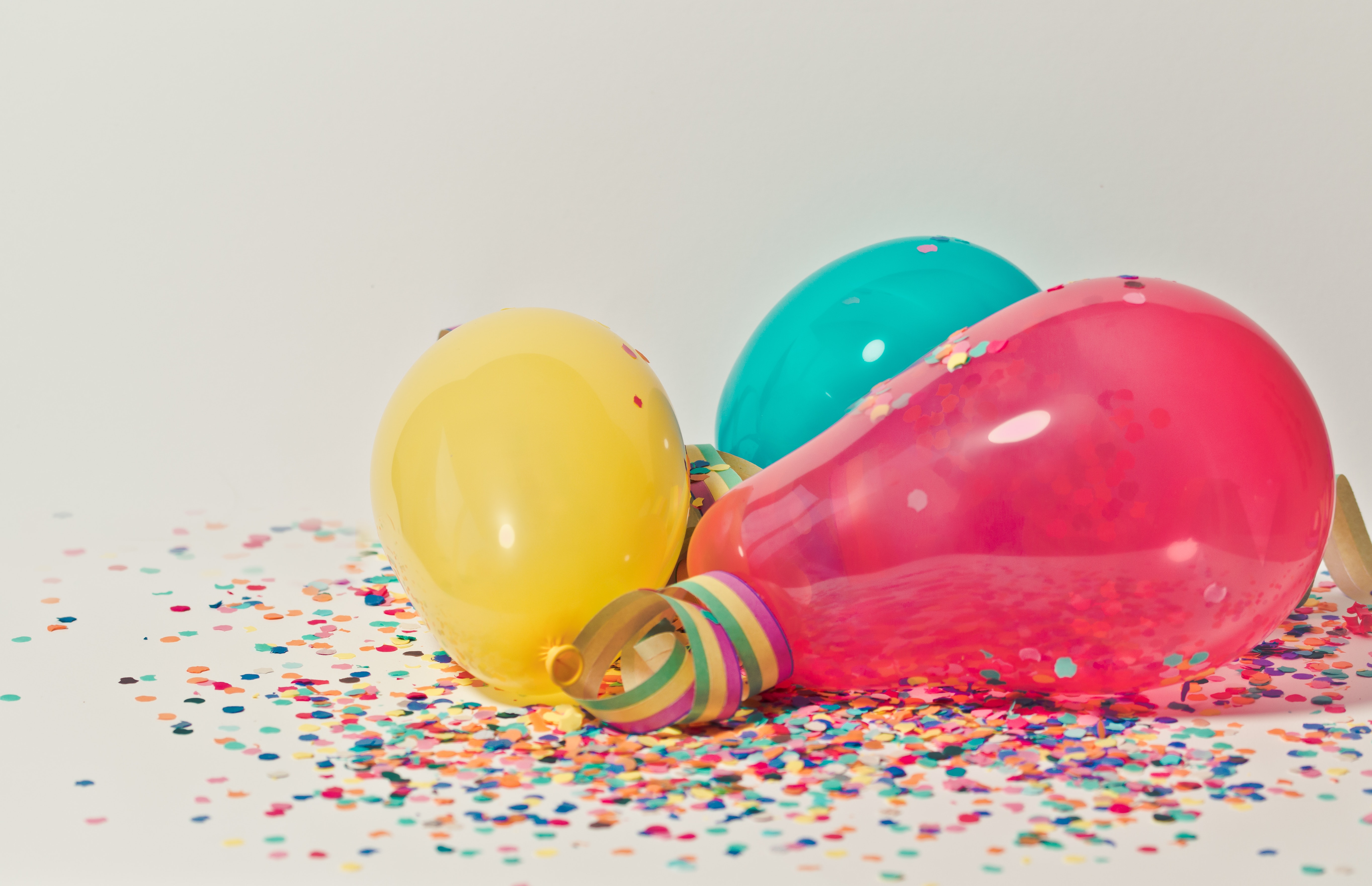 Yellow, teal and pink balloons against a confetti background.