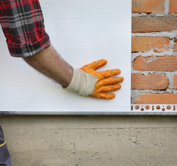 Close-up photograph of a construction worker fitting insulating board on a brick wall