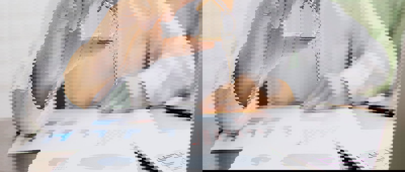 Photograph of someone holding a key with a house-shaped keyring over financial charts