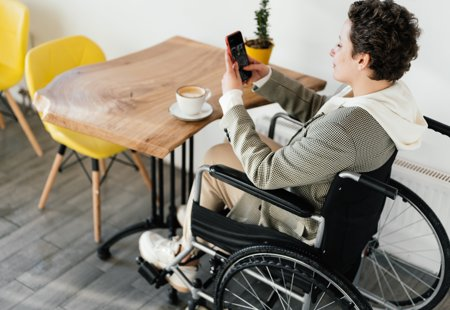 A woman in a wheelchair uses her phone at a table in a cafe.