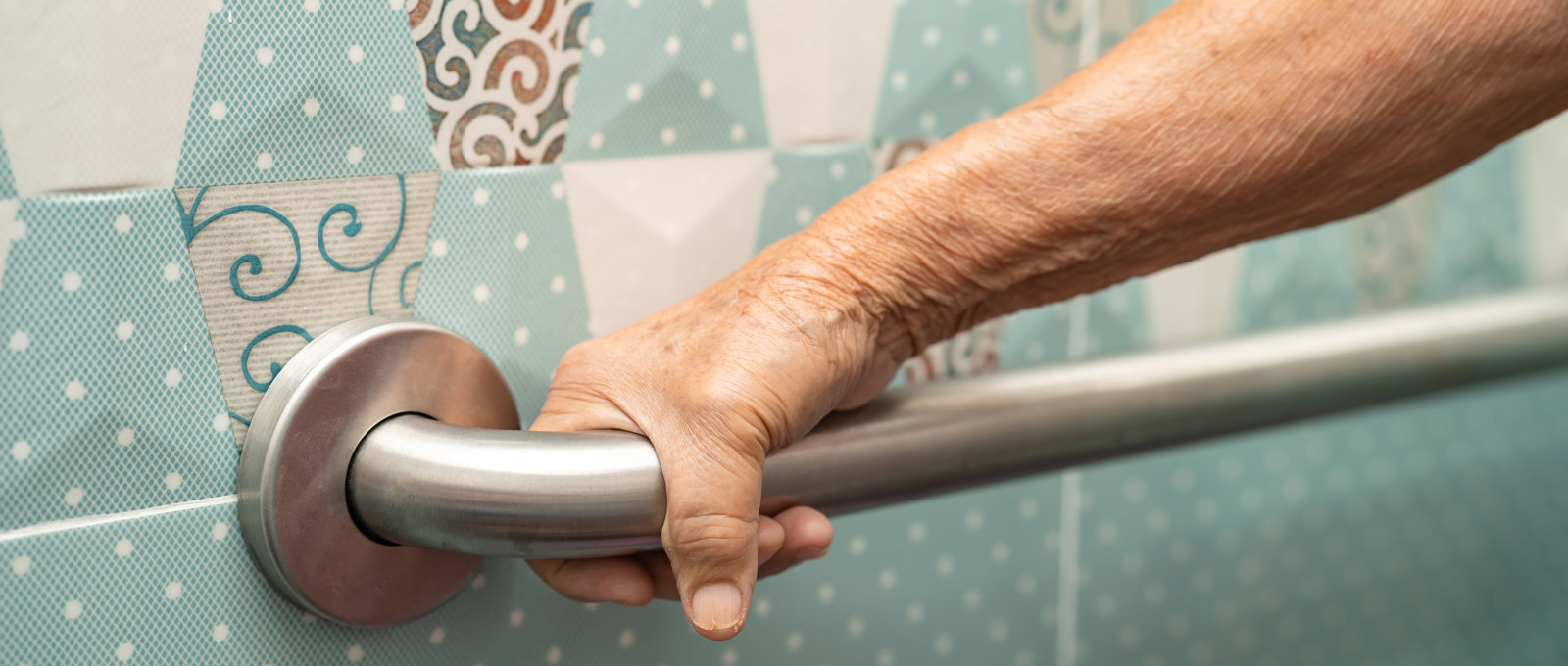 Close-up photo of an elderly woman's hand holding a handrail on a tiled wall