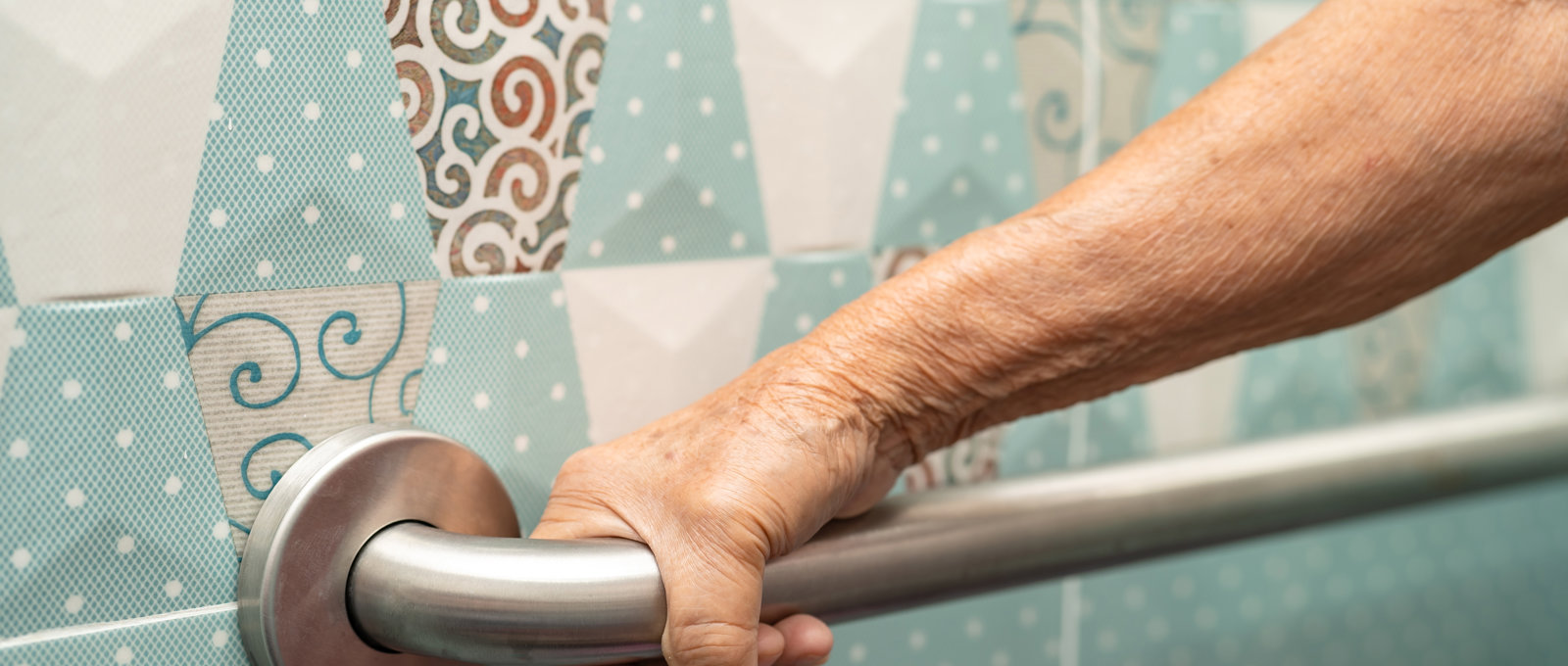 Close-up photo of an elderly woman's hand holding a handrail on a tiled wall