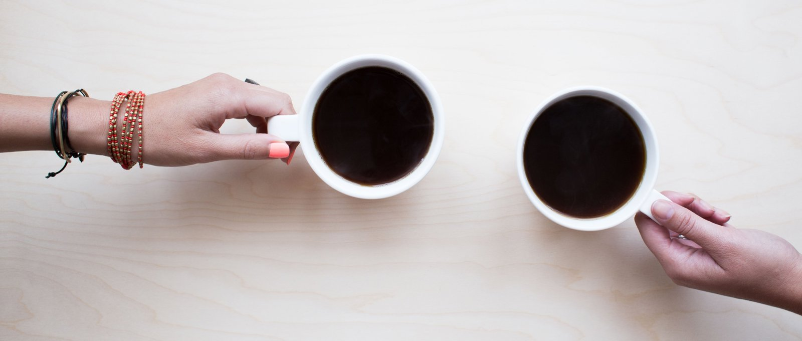 A shot from above of two mugs of black coffee, with a hand resting on each mug