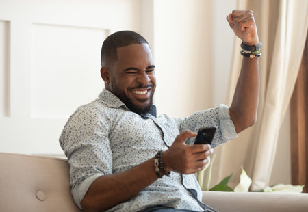 Photograph of a smiling man holding a smart phone and punching the air