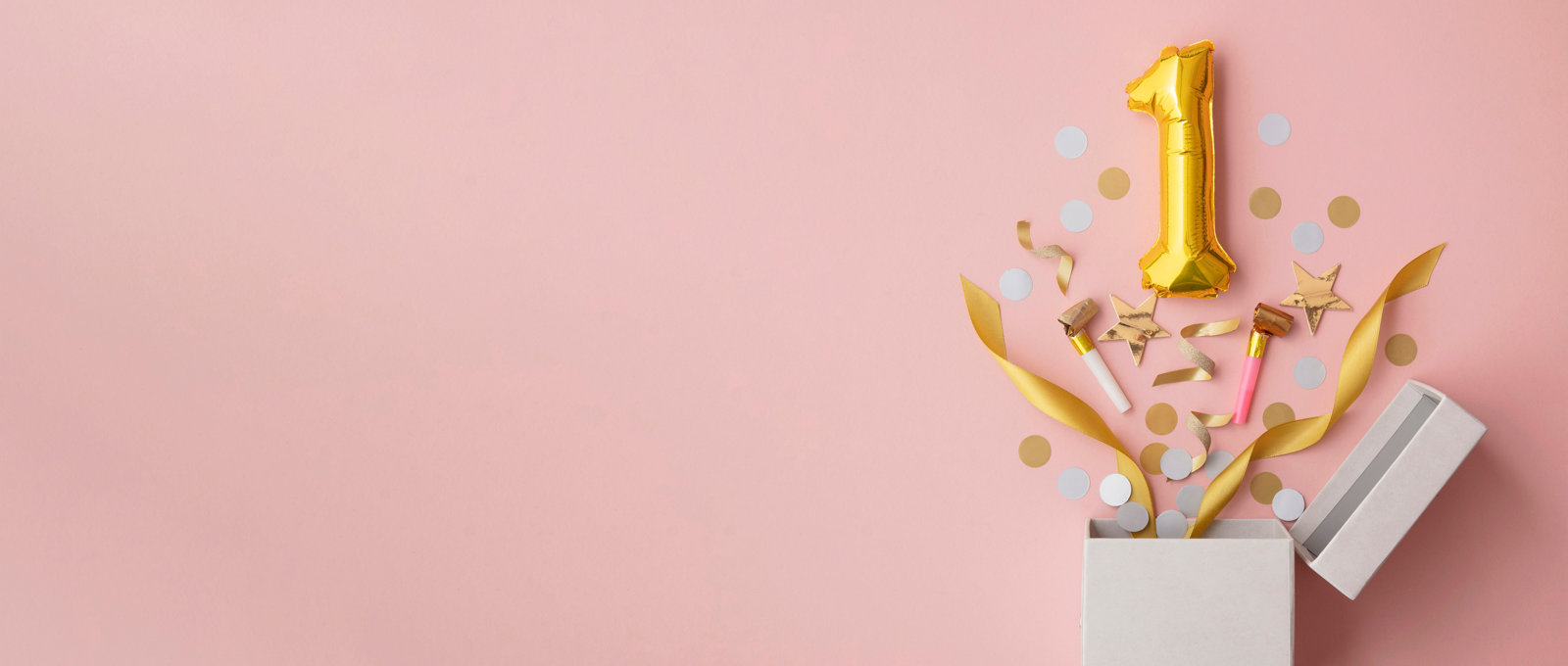 Photograph of a gold balloon in the shape of the number 1 popping out of a box together with ribbons and confetti
