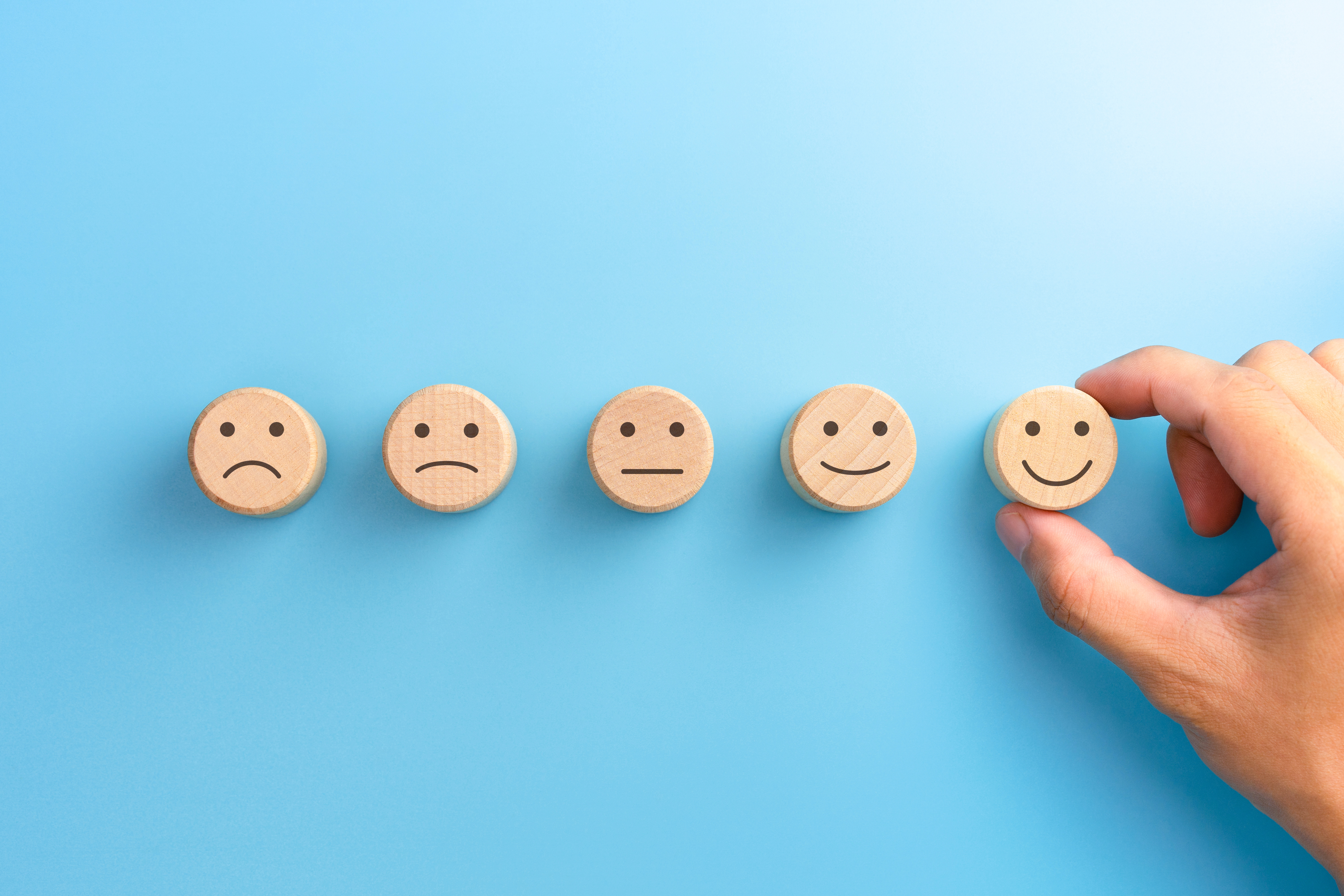 Photograph of five small wooden disks each printed with a face. The range from unhappy to happy expressions going from left to right. 