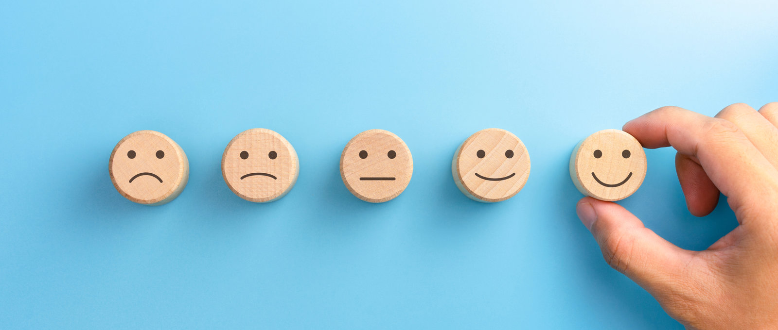Photograph of five small wooden disks each printed with a face. The range from unhappy to happy expressions going from left to right. 