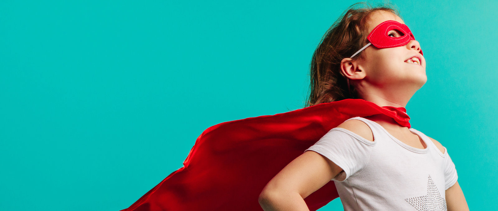 Photo of a young girl as a superhero - wearing a cape and red eye mask