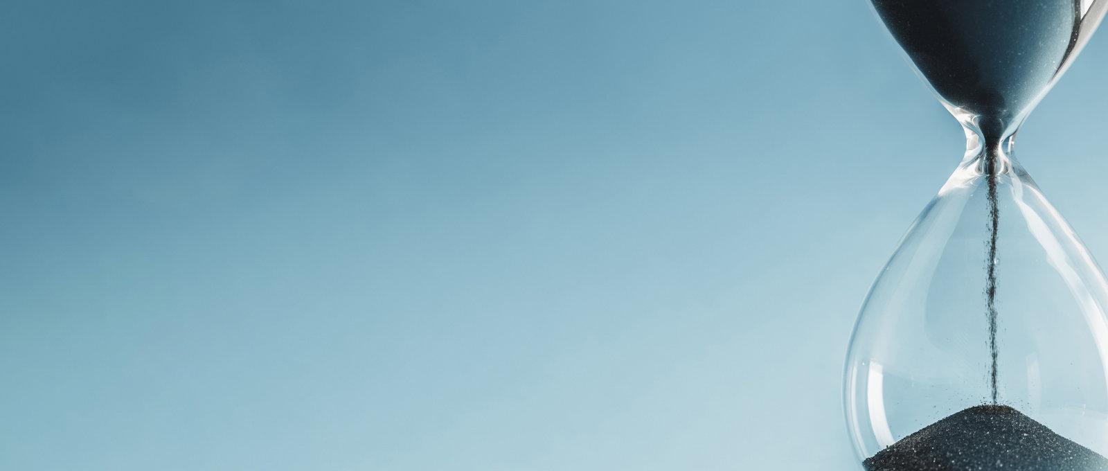 Close-up of black sand flowing down inside an hourglass