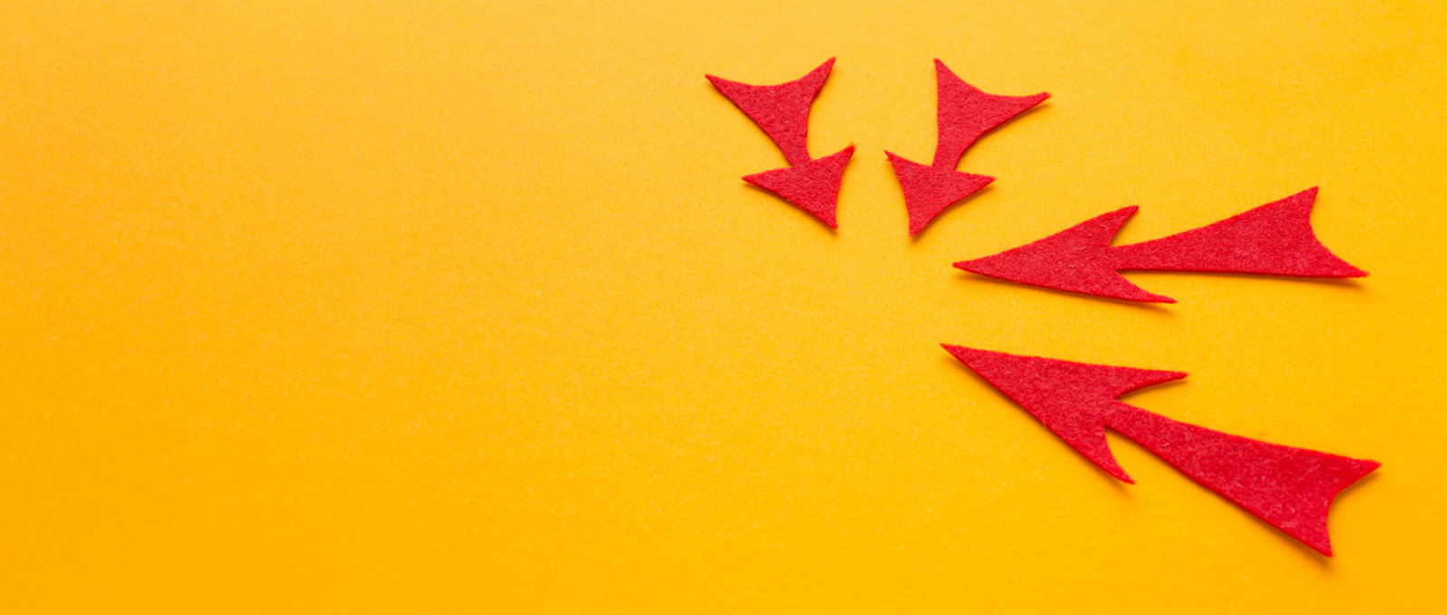 Photo of four red arrows made of felt arranged in a circle, all pointing inwards, on a yellow surface