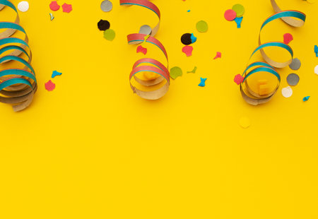 Different coloured spiralling steamers and paper confetti on a yellow surface