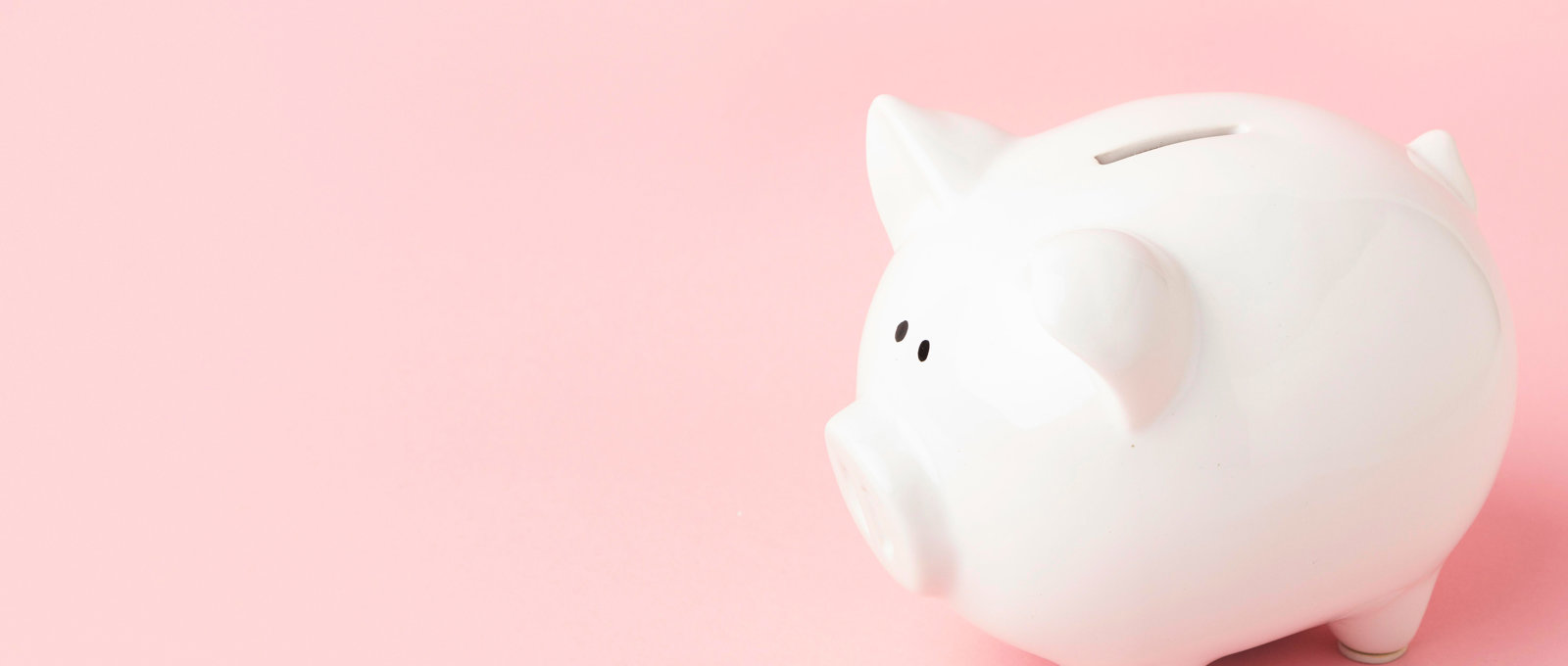 Close-up photo of a white ceramic piggy bank on a pink surface