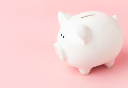 Close-up photo of a white ceramic piggy bank on a pink surface