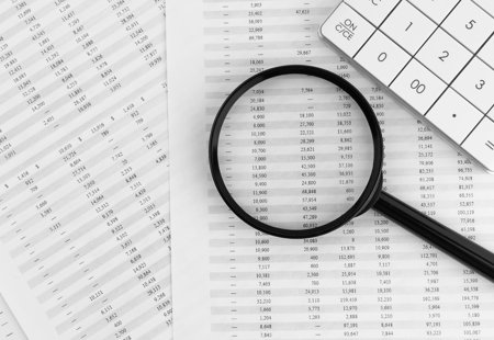 Magnifying glass and calculator sitting on top of printed spreadsheets spread out on a table