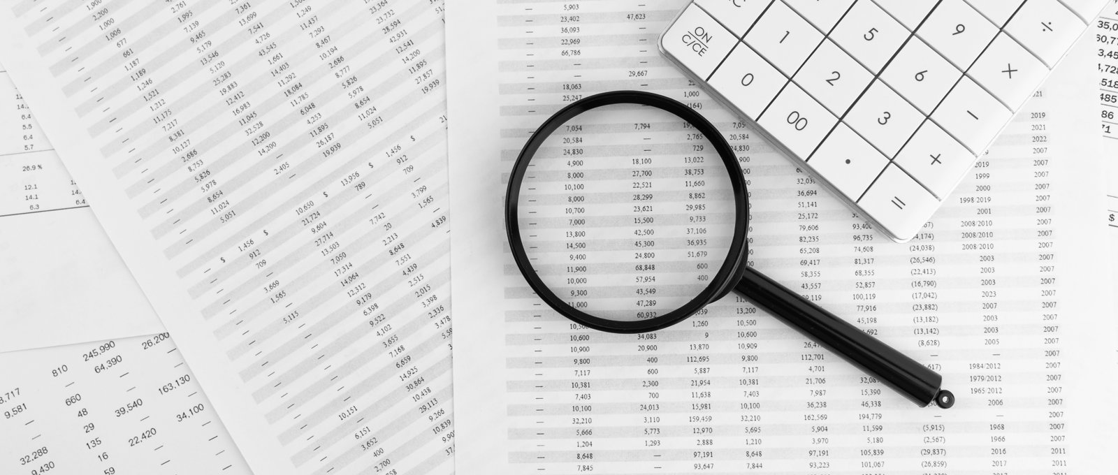 Magnifying glass and calculator sitting on top of printed spreadsheets spread out on a table