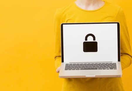 Photograph of a woman wearing yellow clothes against a yellow background. She is holding a laptop. On the screen is a padlock symbol.