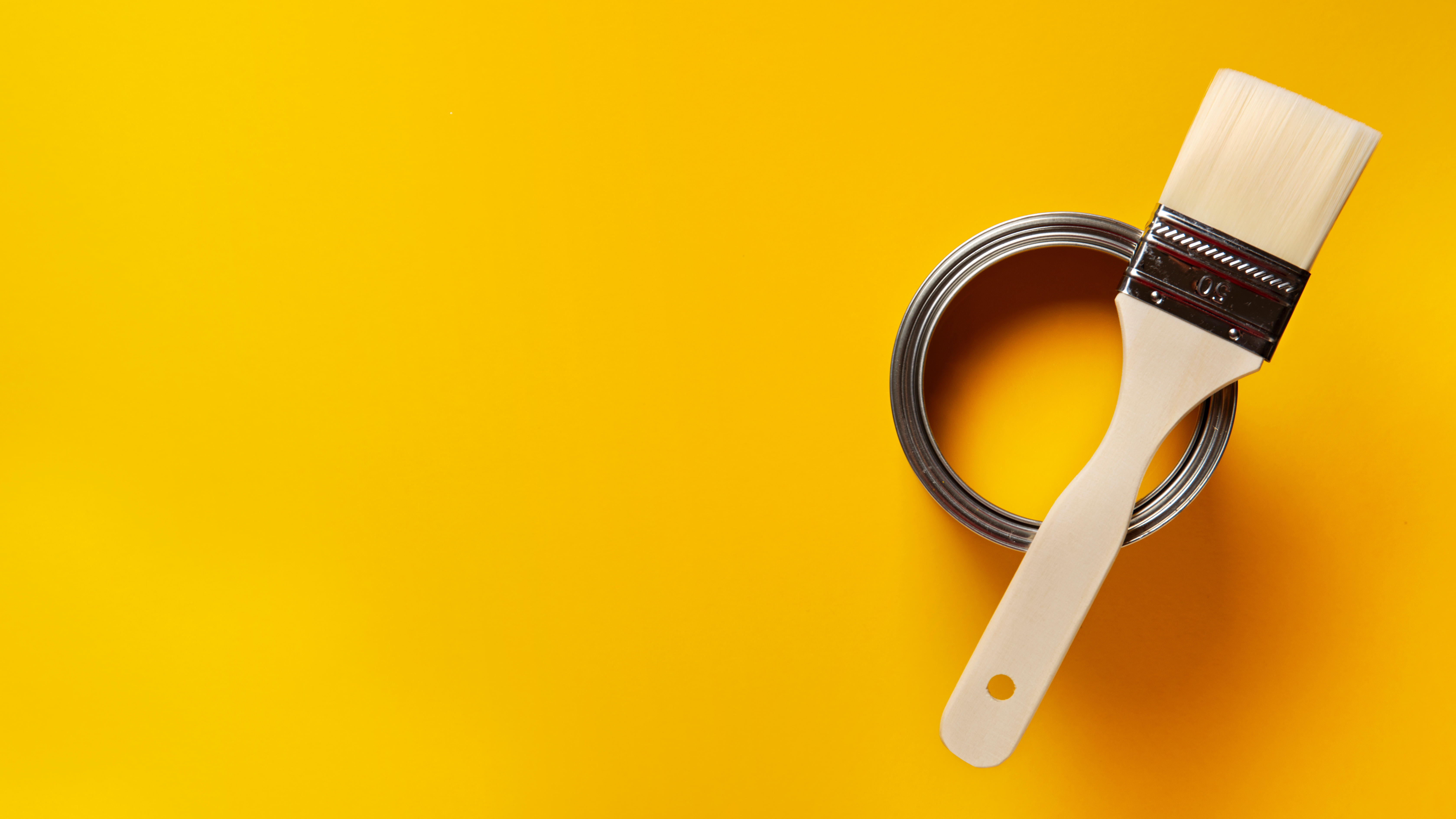 Stylised photo of a paintbrush sitting across the top of an open can of orange paint - all sitting on an orange surface