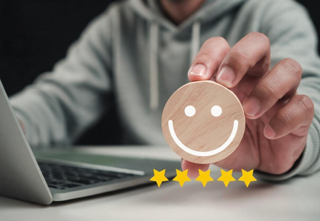 Photo of a hand holding a wooden circle with a smiley face on it and five yellow stars below. 