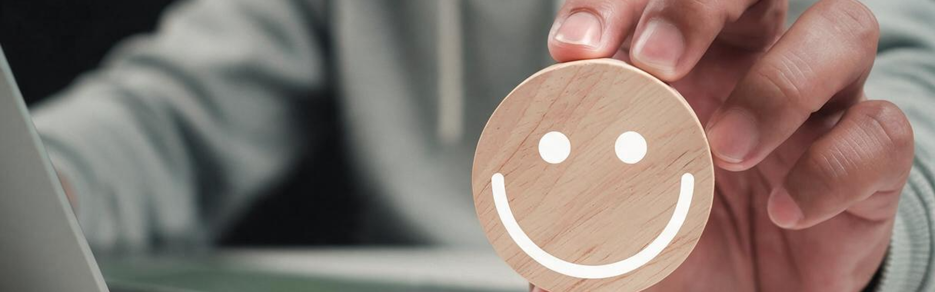 Photo of a hand holding a wooden circle with a smiley face on it and five yellow stars below. 