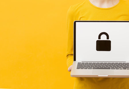 Photograph of a woman wearing yellow clothes against a yellow background. She is holding a laptop. On the screen is a padlock symbol.