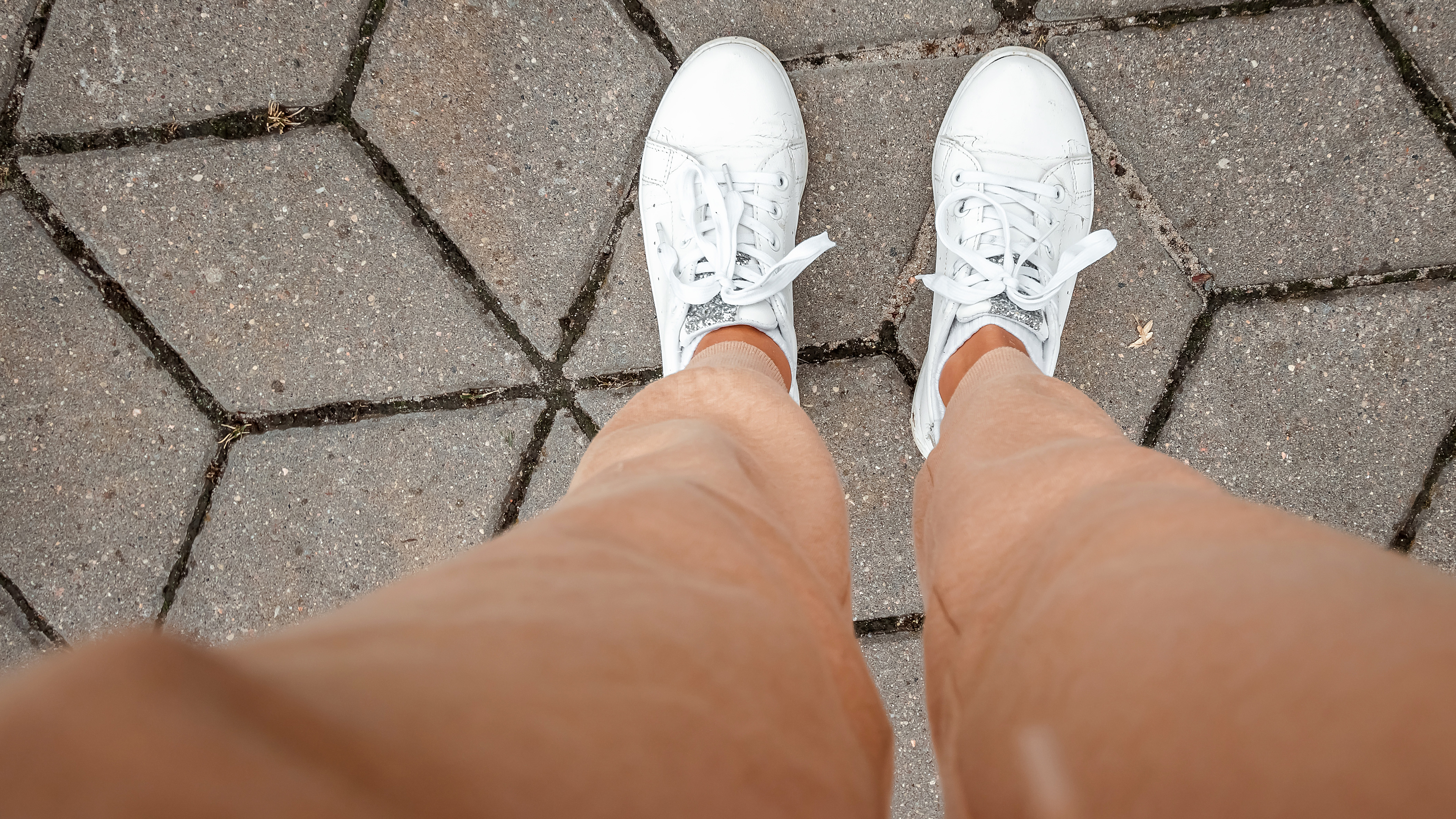 Photograph of a woman's feet on the ground in white trainers, shot looking down