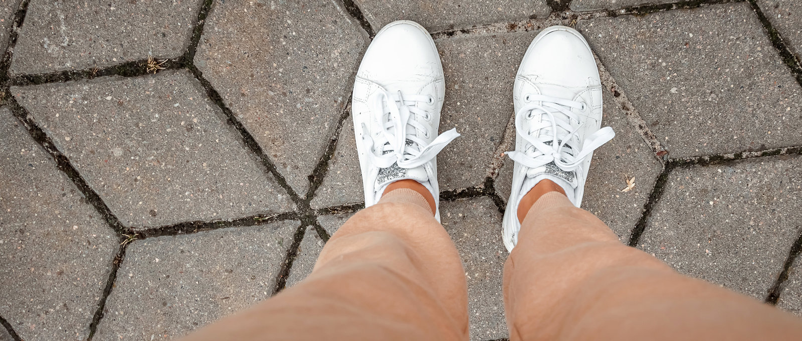 Photograph of a woman's feet on the ground in white trainers, shot looking down