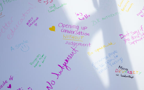 A close up of our pride graffiti wall reading "opening up conversation without judgement" in bright purple handwriting