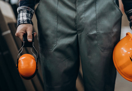 Construction worker holding safety earphones and helmet