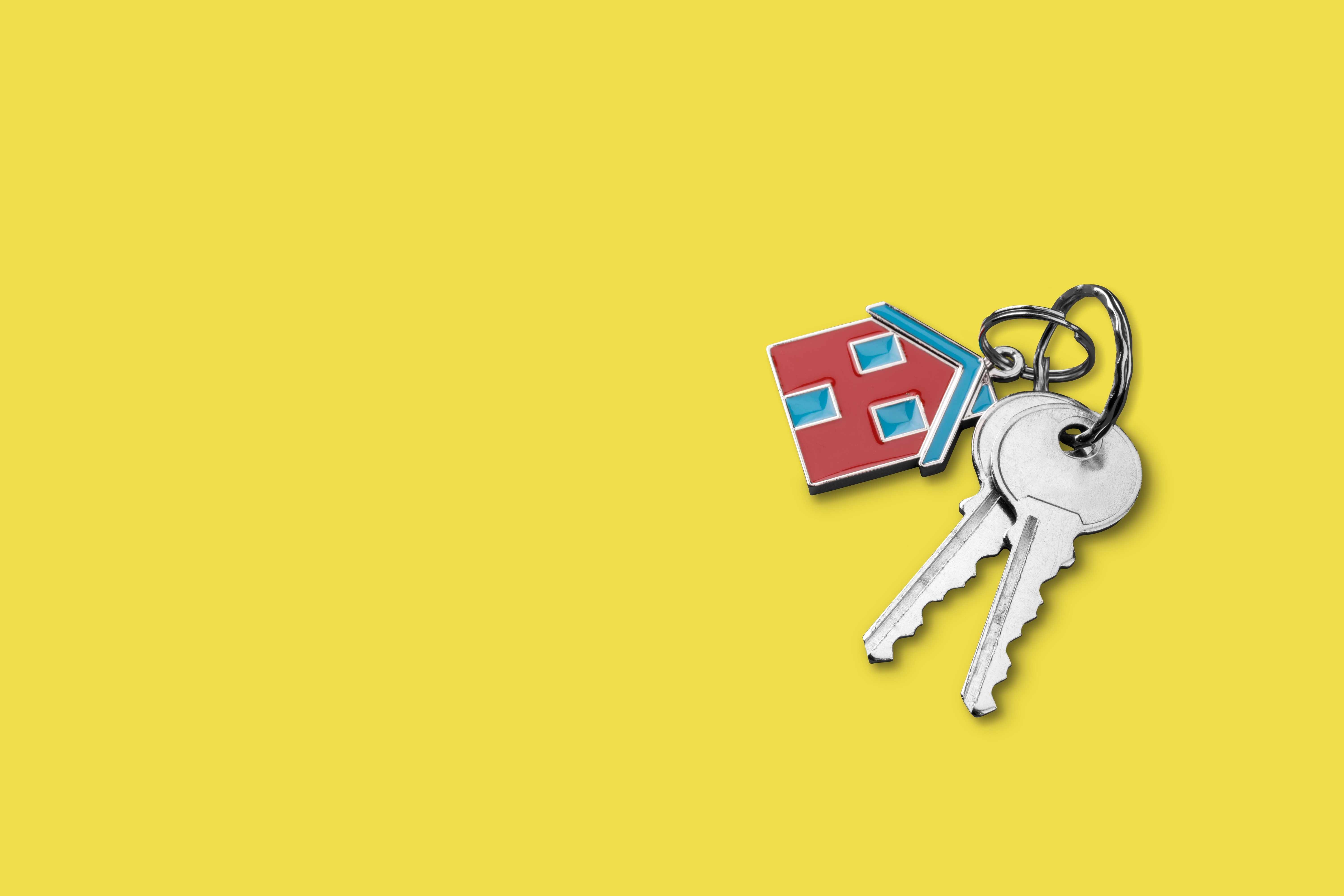 Photograph of two keys attached to a house-shaped keyring, lying on a yellow surface