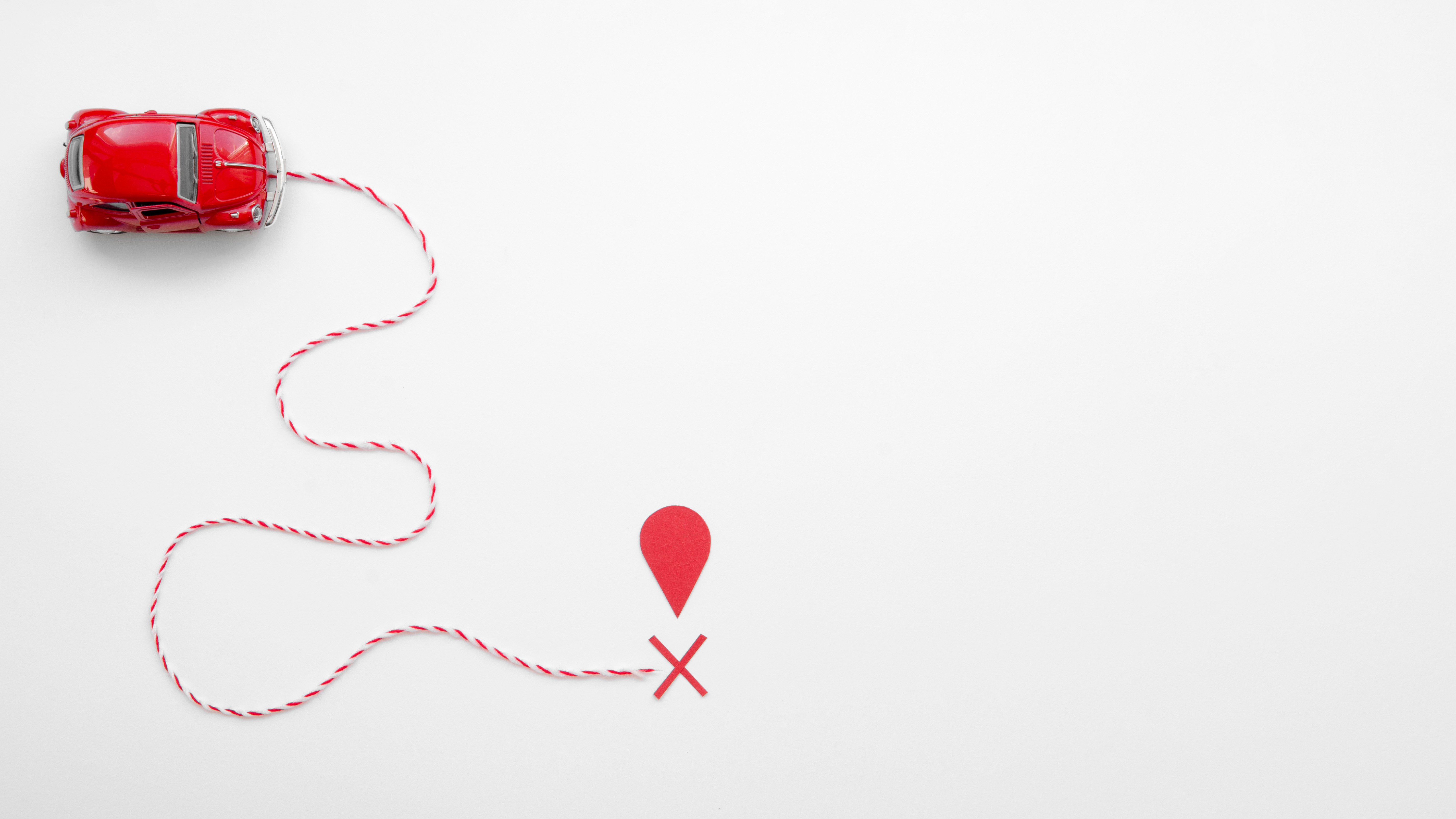 Ariel view of model red toy car connected to a red map point by a winding piece of red and white twisted string