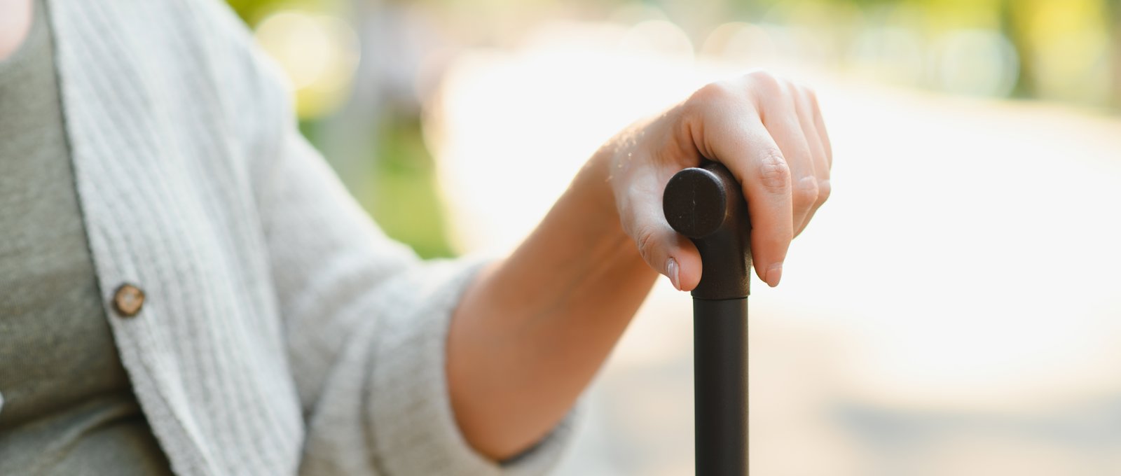 Close up photo of an elderly woman's hand resting on the handle of her walking stick
