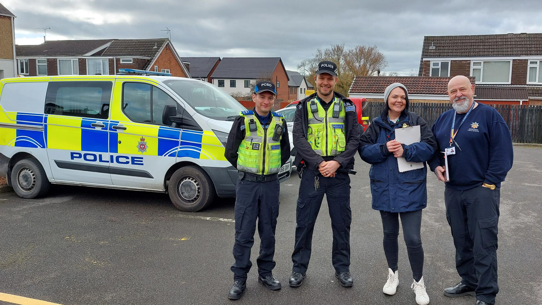 Photo of two Futures team members with two police officers, standing near some Futures homes with a police car in the background