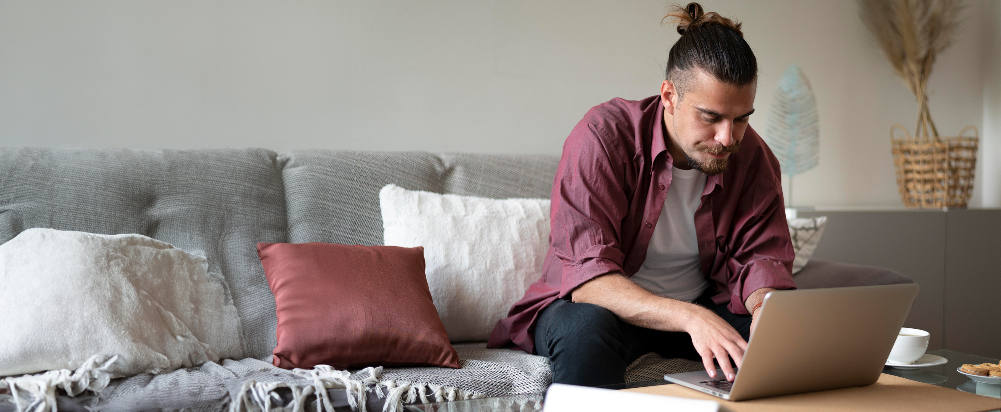 photo of a man sitting on a sofa and using a laptop on a low table in front of him