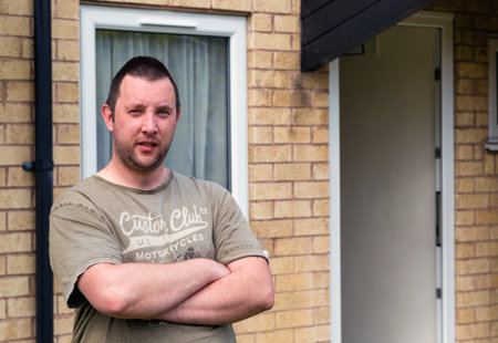 Portrait of Daniel Morris standing with his arms folded outside his home