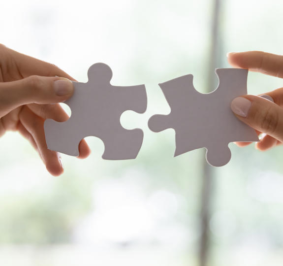 Close up photo of two hands trying to fit two large jigsaw pieces together 